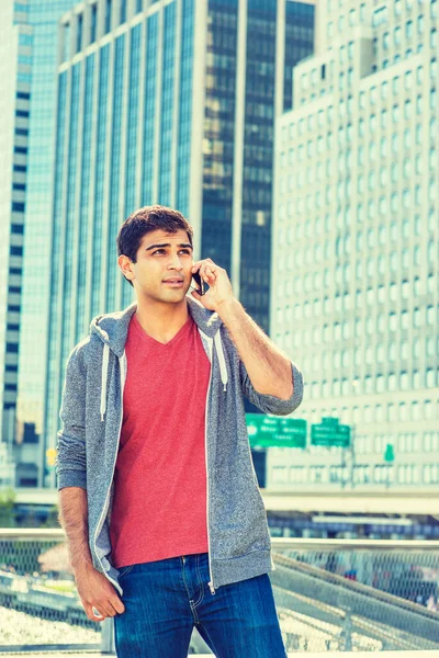 Genç yakışıklı Doğu Hintli Amerikalı adam New York 'a seyahat ediyor. Kırmızı yaka tişörtlü, gri kapüşonlu, iş yerinin önünde dikilen, kafasını kaldırıp telefonla konuşan bir adam.. 