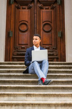 Başarının yolu. New York 'ta okuyan Afro-Amerikan üniversite öğrencisi, mavi ceket, gri pantolon, kırmızı çorap, spor ayakkabı, bacak bacak üstüne atma, merdivenlerde oturmak, dizüstü bilgisayarla çalışmak,