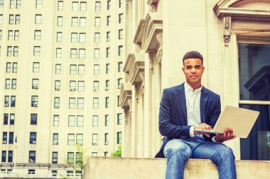 New York 'ta okuyan Afro-Amerikan üniversite öğrencisi, mavi ceketli, gri pantolonlu, ofis binasının dışında oturan, dizüstü bilgisayarla çalışan,. 