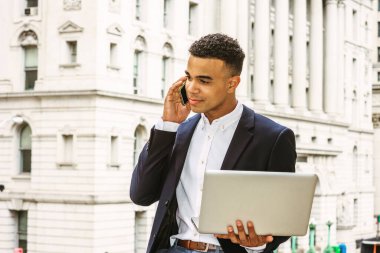 New York 'ta çalışan Afro-Amerikalı iş adamı, siyah ceket giyiyor, beyaz gömlek giyiyor, klasik ofis binasının yanında oturuyor, dizüstü bilgisayarla çalışıyor, cep telefonuyla konuşuyor.. 