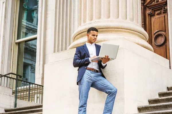 Başarının yolu. New York 'ta okuyan Afro-Amerikan üniversite öğrencisi, mavi ceketli, beyaz gömlekli, gri pantolonlu, ofis binasının önünde duran, dizüstü bilgisayarla çalışan