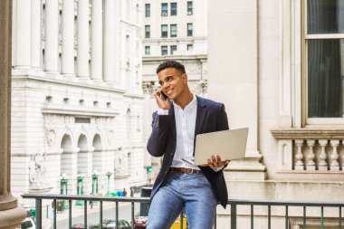 Afrikalı Amerikalı iş adamı New York 'ta çalışıyor. Siyah ceketli, beyaz gömlekli, caddede klasik ofis binasının yanında oturan, dizüstü bilgisayarda çalışan, cep telefonuyla konuşan genç bir adam.. 