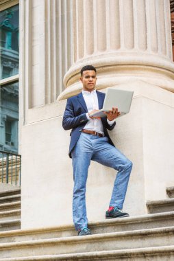 Afrikalı Amerikalı üniversite öğrencisi New York 'ta okuyor. Mavi ceketli, beyaz gömlekli, gri pantolonlu, spor ayakkabılı, genç, ofis binasının dışındaki sütuna karşı merdivenlerde duruyor, dizüstü bilgisayarda çalışıyor..