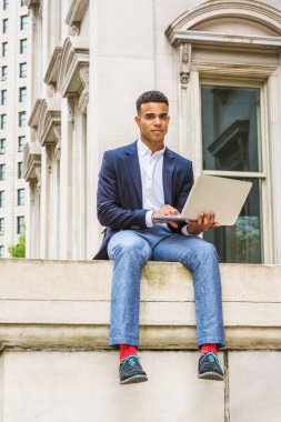 Afrikalı Amerikalı üniversite öğrencisi New York 'ta okuyor. Mavi ceketli, pantolonlu, kırmızı çoraplı, spor ayakkabılı kampüsteki klasik ofis binasının önünde oturan, okuyan, dizüstü bilgisayarda çalışan bir adam..