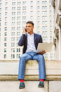 Afrikalı Amerikalı üniversite öğrencisi New York 'ta okuyor. Mavi ceketli, gri pantolonlu, beyaz gömlekli, kırmızı çoraplı, spor ayakkabılı, ofisin dışında oturan, dizüstü bilgisayarda çalışan, telefonla konuşan bir adam..