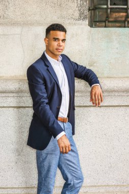 New York 'ta Afro-Amerikan bir gencin portresi. Mavi ceketli, beyaz tişörtlü, siyahi bir üniversite öğrencisi kampüste klasik duvara karşı duruyor.. 