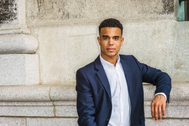 New York 'ta Afro-Amerikan bir gencin portresi. Mavi ceketi, beyaz gömleği, pantolonu, spor ayakkabısı olan siyah bir üniversite öğrencisi kampüste klasik duvarın karşısında duruyor. Filtrelenmiş etki.