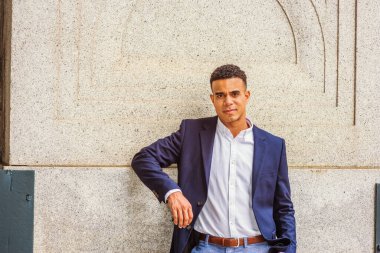 New York 'ta Afro-Amerikan bir gencin portresi. Mavi ceketli, beyaz gömlekli, siyahi bir üniversite öğrencisi kampüste klasik bir duvara karşı duruyor, sana bakıyor.. 