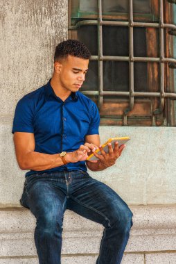 Okumayı seviyorum. Modern okuma. Mavi kısa kollu gömlek, kot pantolon, Afro-Amerikan üniversite öğrencisi New York 'ta eski moda bir duvarın karşısında oturmuş, küçük tablet bilgisayar okuyor..