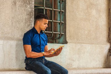 Okumayı seviyorum. Modern okuma. Mavi kısa kollu gömlek, kot pantolon, Afro-Amerikan üniversite öğrencisi New York 'ta eski moda bir duvarın karşısında oturmuş, küçük tablet bilgisayar okuyor..