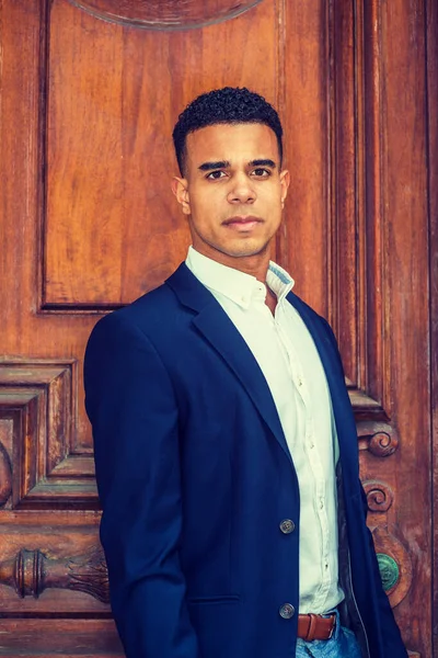Portrait of African American Businessman in New York. Wearing dark blue blazer, white shirt, a male college student stands by vintage office doorway, looking up, thinking.