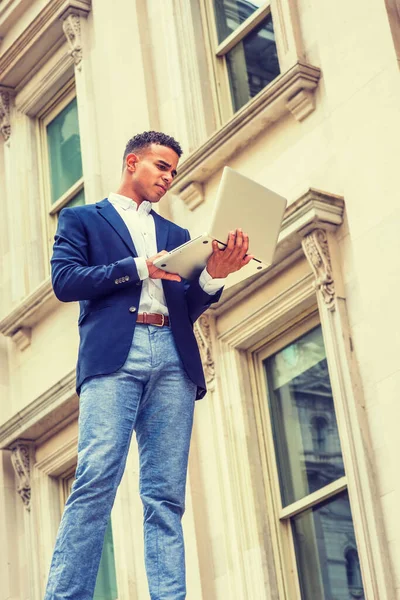 Way to Success. African American college student studies in New York. Wearing blue blazer, white shirt, man stands outside vintage office building, works on laptop computer.