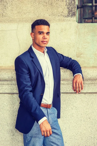 New York 'ta Afro-Amerikan bir gencin portresi. Mavi ceketli, beyaz tişörtlü, siyahi bir üniversite öğrencisi kampüste klasik duvara karşı duruyor.. 