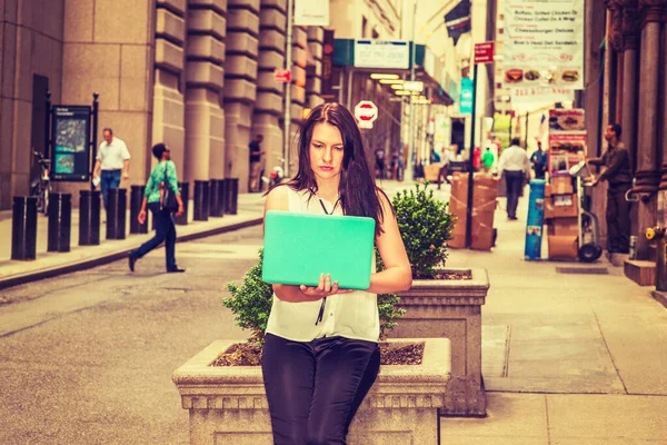 Modern Daily Life in New York. American Woman with long black hair, wearing white sleeveless shirt, sitting on vintage narrow street, reading, working on laptop computer.