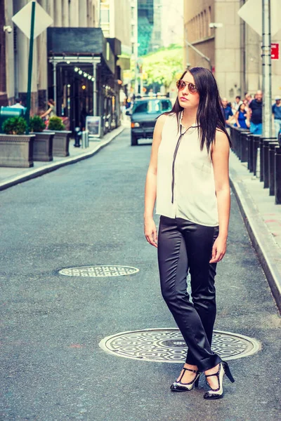 ニューヨークを旅するアメリカ人女性は 白い無色の袖のないシャツ 黒のパンツ ヒール サングラスを身に着けて ヴィンテージストリートに立って 周りを見回します バックグラウンドで人々 — ストック写真