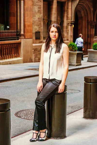 夏にニューヨークを旅する長い黒い髪をしたアメリカの女性は 白無色のノースリーブシャツ 黒いパンツ かかと ヴィンテージストリートの金属の柱に座って リラックスした — ストック写真