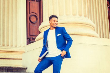 New York 'ta çalışan Afrikalı Amerikalı iş adamı. Mavi takım elbiseli, beyaz tişörtlü, küçük keçi sakallı üniversite öğrencisi, kampüsün klasik kapısında duruyor, dizüstü bilgisayar taşıyor, gülümsüyor.