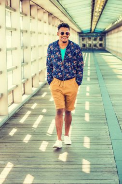 Afro-Amerikan üniversite öğrencisi, mavi desenli ceket, sarı kahverengi şort, beyaz spor ayakkabı, güneş gözlüğü, yürüyen cam duvarlar, tavan, New York 'ta kampüste ahşap zemin..