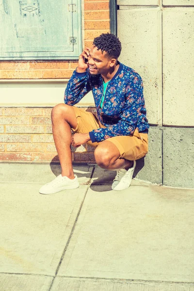 アフリカ系アメリカ人の男性はニューヨークに旅行し 青いパターンのジャケット 黄色の茶色のショートパンツ 白いスニーカーを着て 通りの隅に不法占拠 携帯電話で話しています 現代の生活 — ストック写真