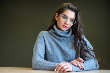 Gözlüklü zarif, ince bir kadın ve arka planda gri bir süveter ve fotokopi alanı var.