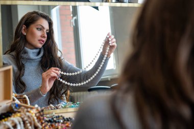 Aynada farklı takıları seçen ve deneyen bir kadının yansıması, yumuşak odak, yakın plan