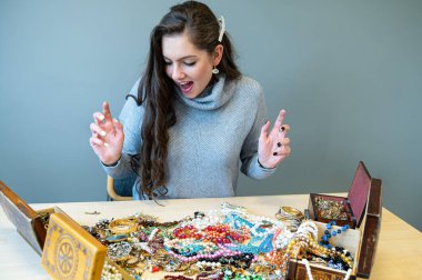 Masada bir sürü mücevherle oturan ince esmer, farklı mücevherler seçiyor ve deniyor.