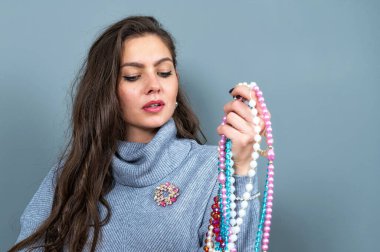 Uzun gri kazaklı sıska kadın, gri renkli kolye ve mücevherlerle eğleniyor.