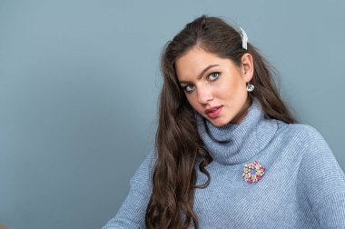 Uzun gri süveterli zarif, ince bir kadın. Fotokopi alanı olan gri bir arka planda izole edilmiş.