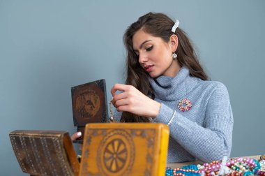 Masada bir sürü mücevherle oturan ince esmer, farklı mücevherler seçiyor ve deniyor.