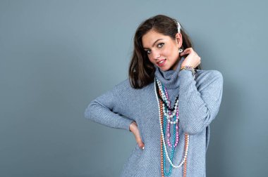 Uzun gri kazaklı sıska kadın, gri renkli kolye ve mücevherlerle eğleniyor.