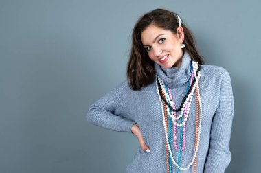 Uzun gri kazaklı sıska kadın, gri renkli kolye ve mücevherlerle eğleniyor.