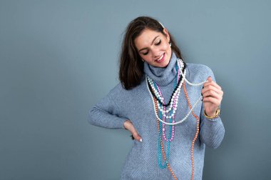 Uzun gri kazaklı sıska kadın, gri renkli kolye ve mücevherlerle eğleniyor.