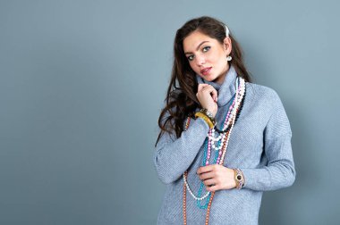 Uzun gri kazaklı sıska kadın, gri renkli kolye ve mücevherlerle eğleniyor.