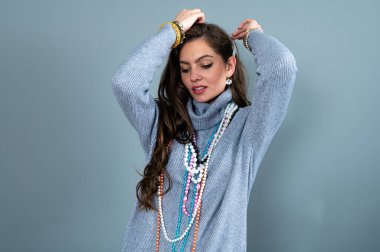 Uzun gri kazaklı sıska kadın, gri renkli kolye ve mücevherlerle eğleniyor.