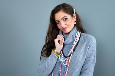 Uzun gri kazaklı sıska kadın, gri renkli kolye ve mücevherlerle eğleniyor.