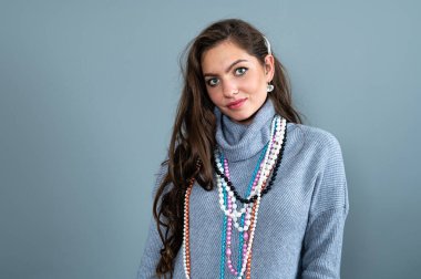 Uzun gri kazaklı sıska kadın, gri renkli kolye ve mücevherlerle eğleniyor.