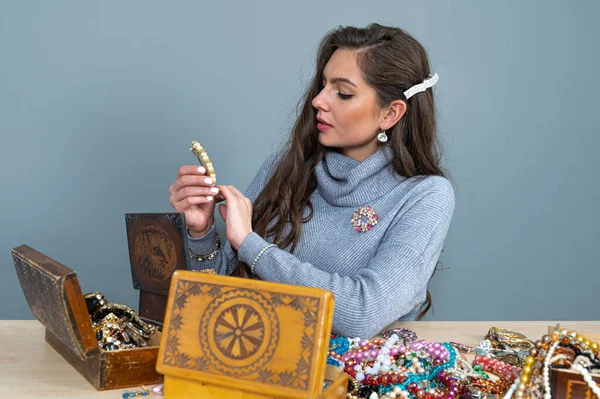 Masada bir sürü mücevherle oturan ince esmer, farklı mücevherler seçiyor ve deniyor.
