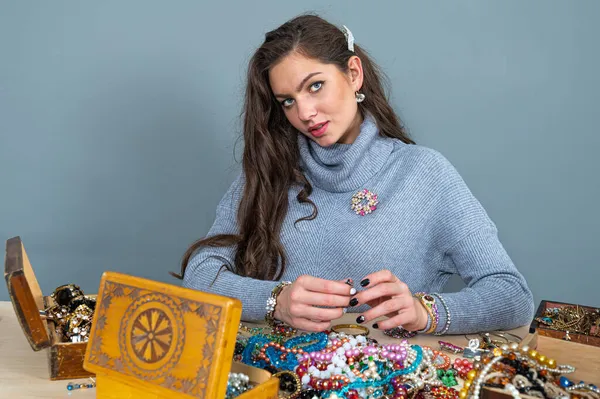 Masada bir sürü mücevherle oturan ince esmer, farklı mücevherler seçiyor ve deniyor.