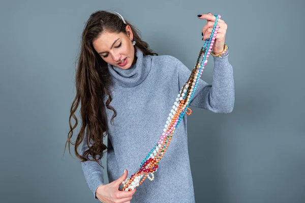 Uzun gri kazaklı sıska kadın, gri renkli kolye ve mücevherlerle eğleniyor.