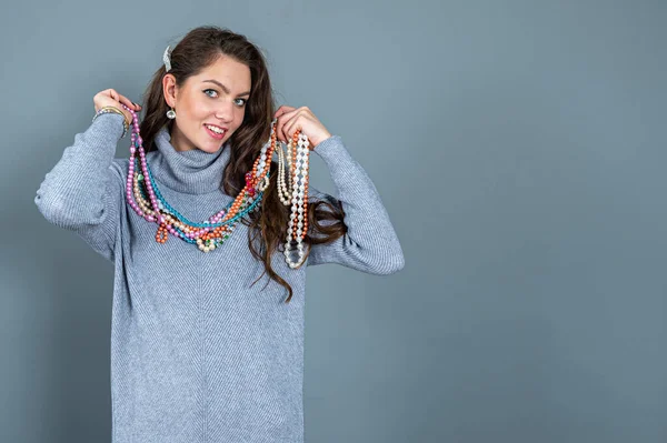 Uzun gri kazaklı sıska kadın, gri renkli kolye ve mücevherlerle eğleniyor.