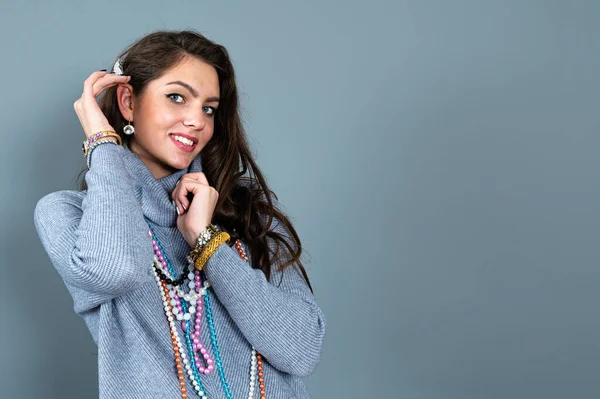 Uzun gri kazaklı sıska kadın, gri renkli kolye ve mücevherlerle eğleniyor.