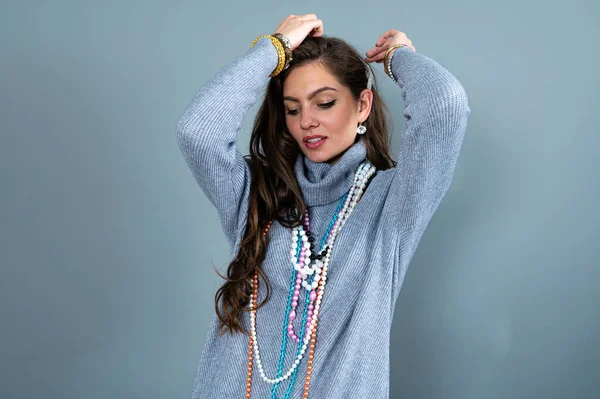 Uzun gri kazaklı sıska kadın, gri renkli kolye ve mücevherlerle eğleniyor.