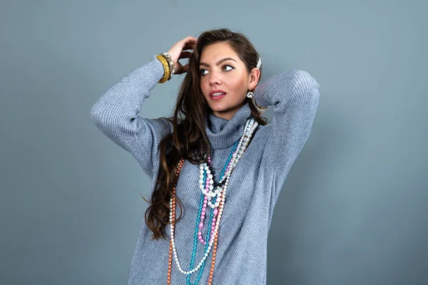 Uzun gri kazaklı sıska kadın, gri renkli kolye ve mücevherlerle eğleniyor.