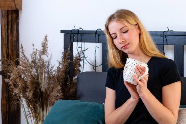 Güzel, genç bir kadın sabah uyandıktan sonra yatakta yatarken kahve ya da çay içiyor.