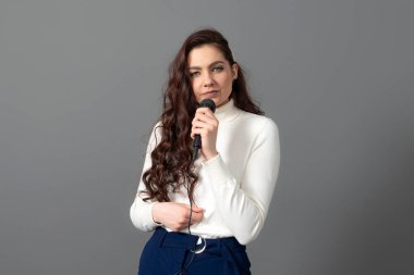 Sunum sırasında çekici kadın konferans konuşmacısı, mikrofonu tutuyor ve gri üzerine izole edilmiş bazı jestler yapıyor.