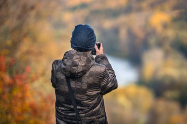 Genç fotoğrafçının arka görüntüsü sonbahar manzarasının fotoğraflarını çekiyor, yakın plan.