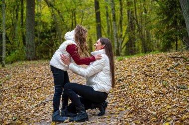 Açık renk ceket giymiş iki kız kardeş sonbaharda ormanda yürürler, konuşurlar ve sırlarını paylaşırlar.