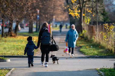 Riga, Letonya, 2 Kasım 2021: Sonbahar şehrinde kaldırımda çocuklu ve köpeği olan bir kadın.