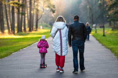 Riga, Letonya, 30 Ekim 2021: Güneşli bir sonbahar öğleden sonrasında çocuklu bir aile parkta yürür.