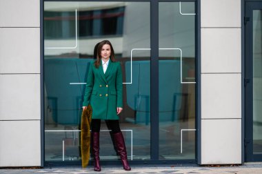 Finans bölgesinde cam kaplı bir binanın yanında zarif giyimli bir iş kadınının portresi.